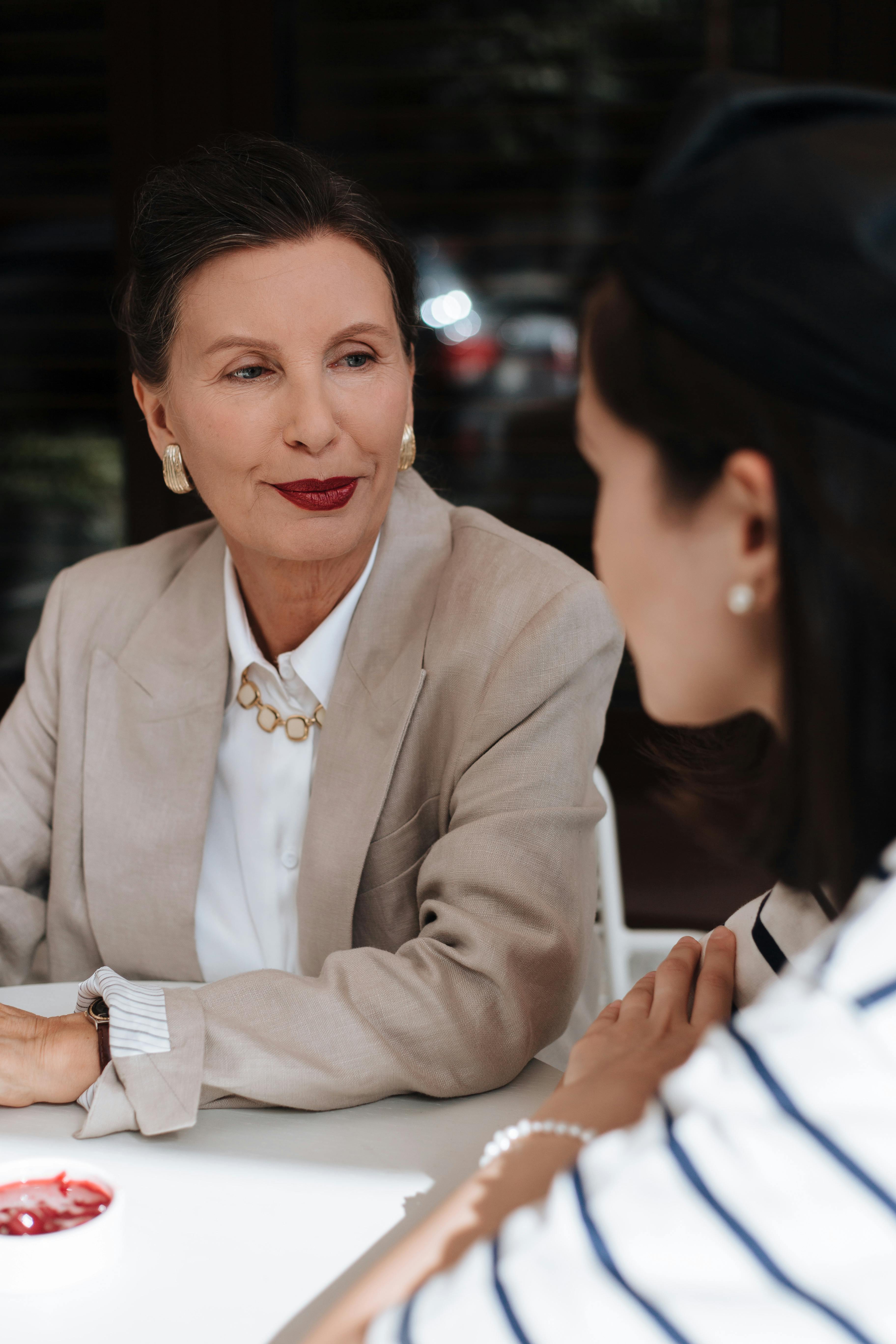 Stylish senior woman in a blazer conversing with another person indoors. Elegant and unique style captured.