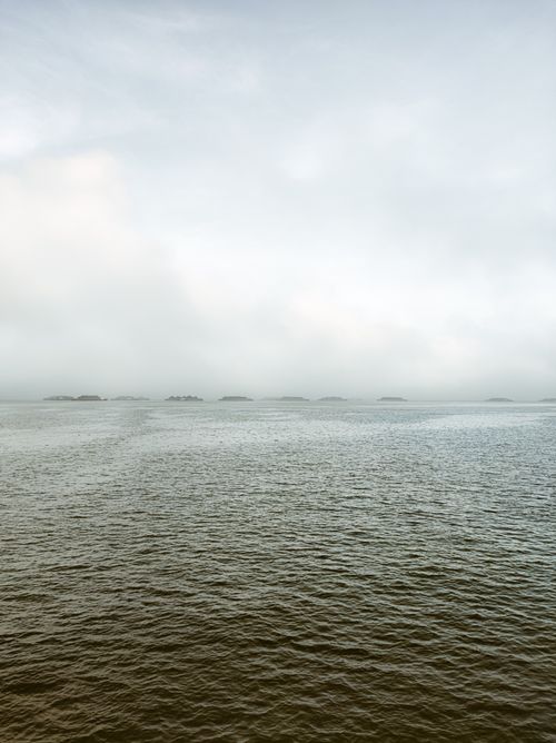 Free Serene view of a calm ocean with a misty horizon and gentle waves under a cloudy sky. Stock Photo
