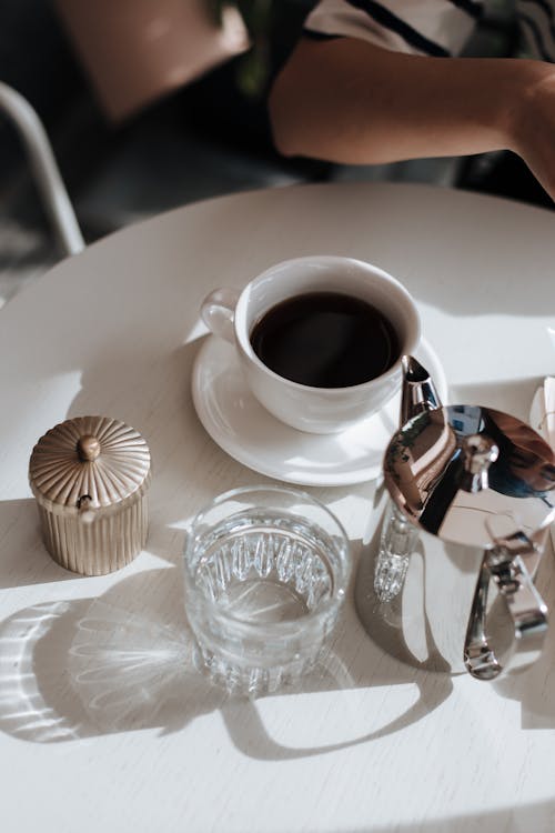 A Person Sitting at the Table with a Cup of Black Coffee