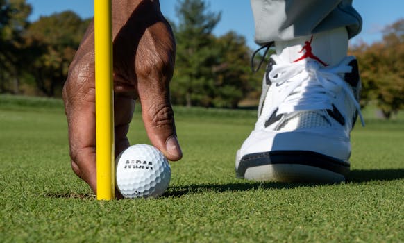 A detailed close-up of a golfer's hand placing a golf ball near the hole on a sunny day.