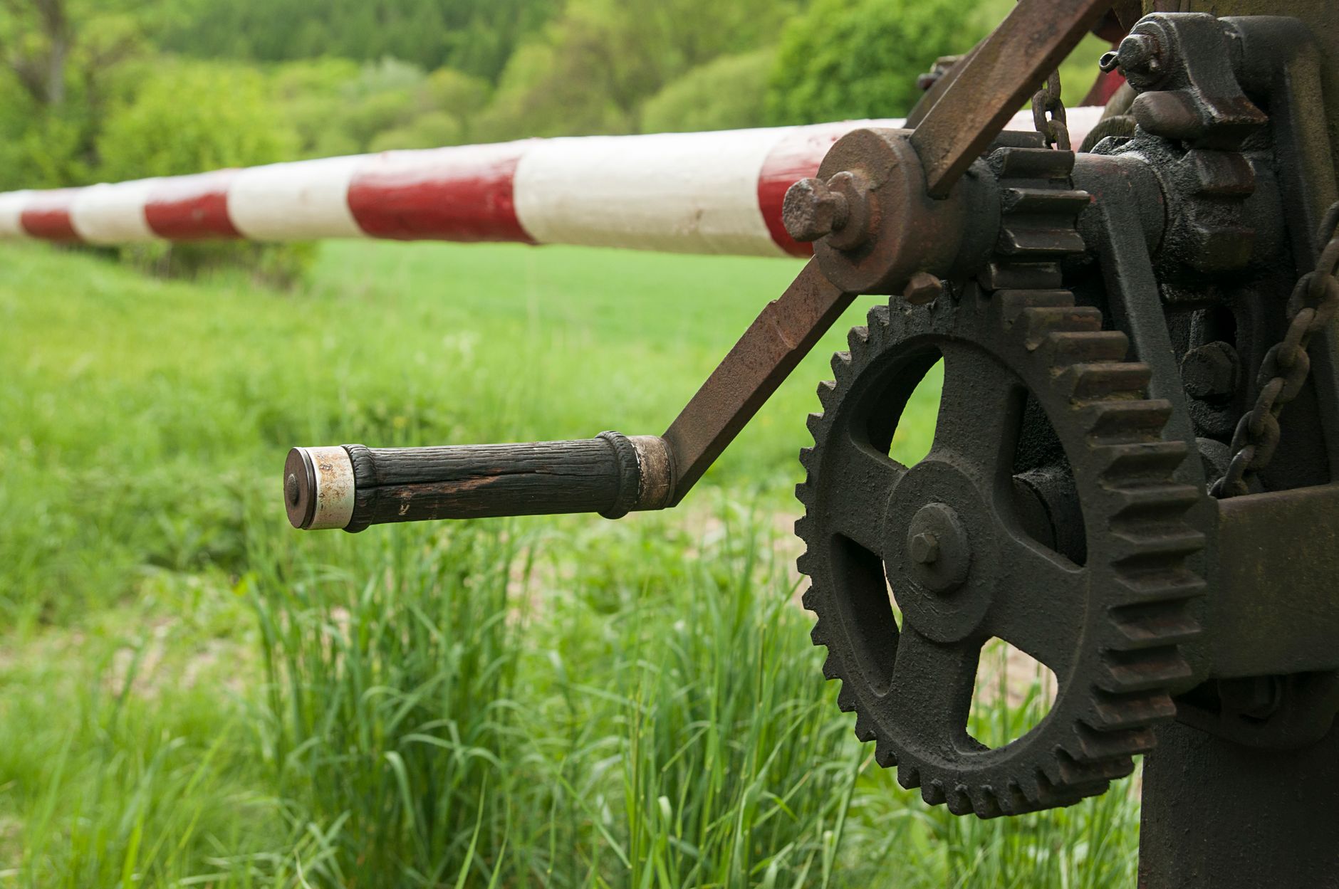 Close-up of a mechanical gear and barrier against a green grassland backdrop.
