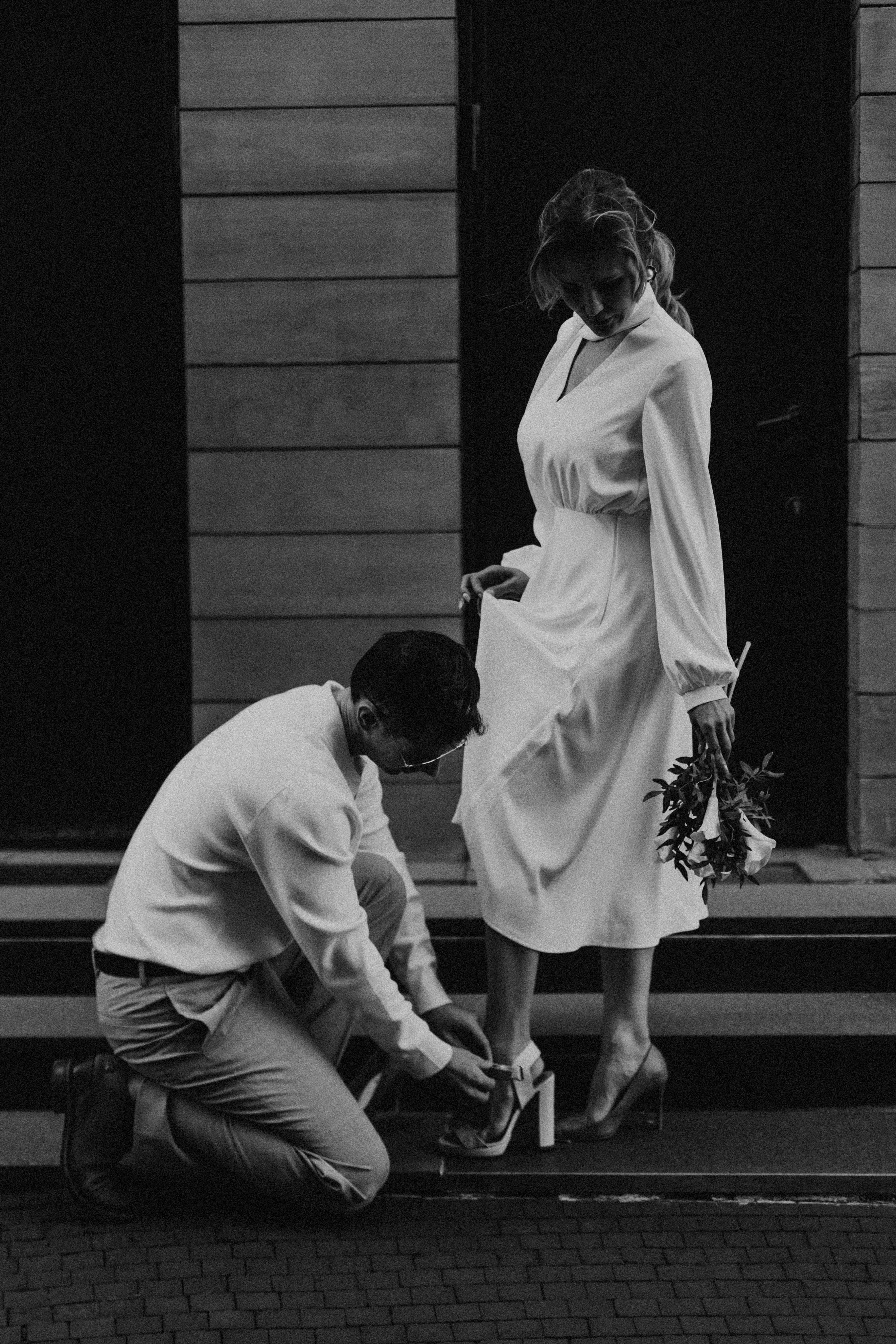 A romantic black and white photo of a couple on their wedding day with the groom kneeling.