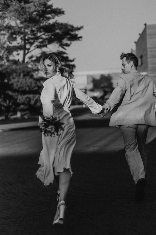 A Grayscale Photo of a Couple Running while Holding Hands