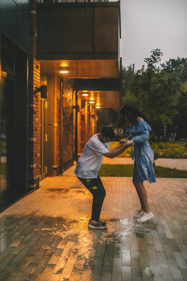 A Couple Jumping On The Puddle Of Water In Front Of The Buildiing