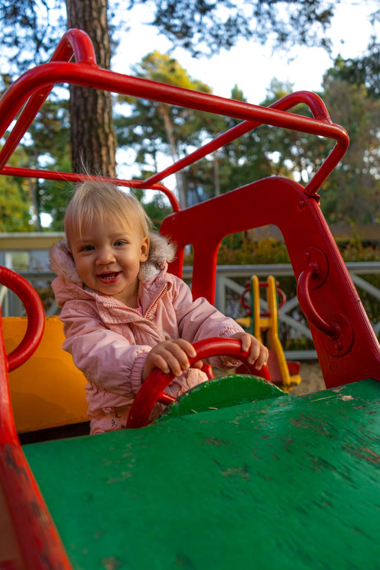 A Baby Girl In Pink Jacket Sitting On The Playground