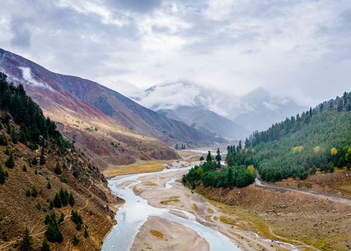 Free Beautiful aerial view of a mountain valley with a winding river and lush forest under a cloudy sky. Stock Photo