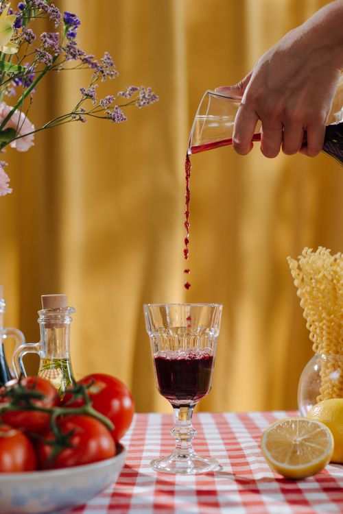 Free A glass of red wine being poured on a table with tomatoes and pasta. Stock Photo