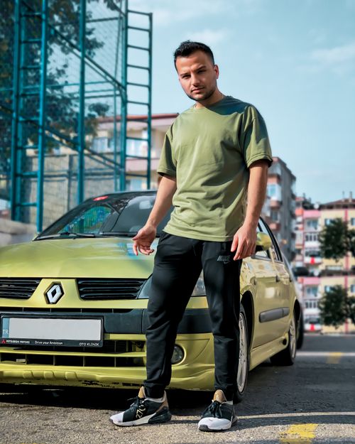 Free Casual young man standing confidently next to a green Renault car in an urban setting. Stock Photo