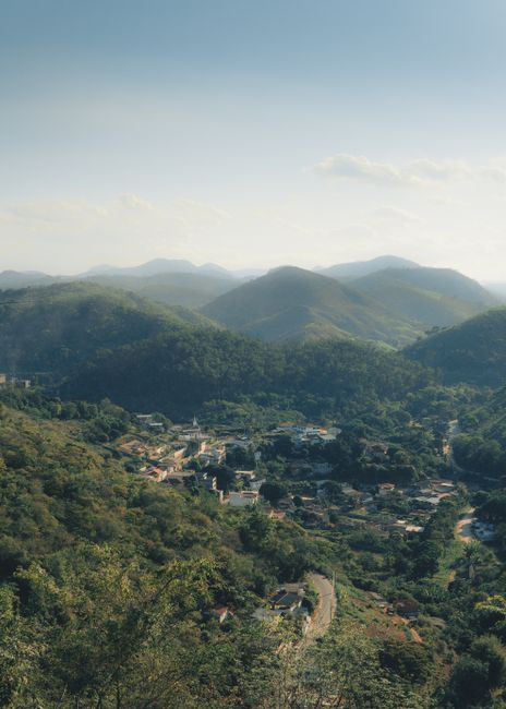 Drone view of lush hills and valley with scattered houses under a blue sky.