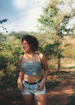 A woman smiling in a gingham top and denim shorts enjoying the outdoors on a sunny day.