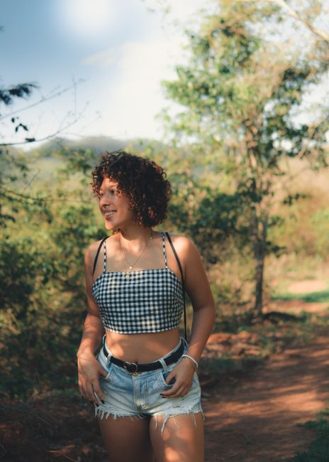 A woman smiling in a gingham top and denim shorts enjoying the outdoors on a sunny day.