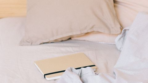 A tranquil bedroom scene with cozy pillows, notebook, and soft bedding.