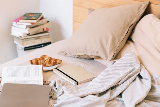 A cozy bed with a croissant, books, and a planner, creating a warm morning vibe.