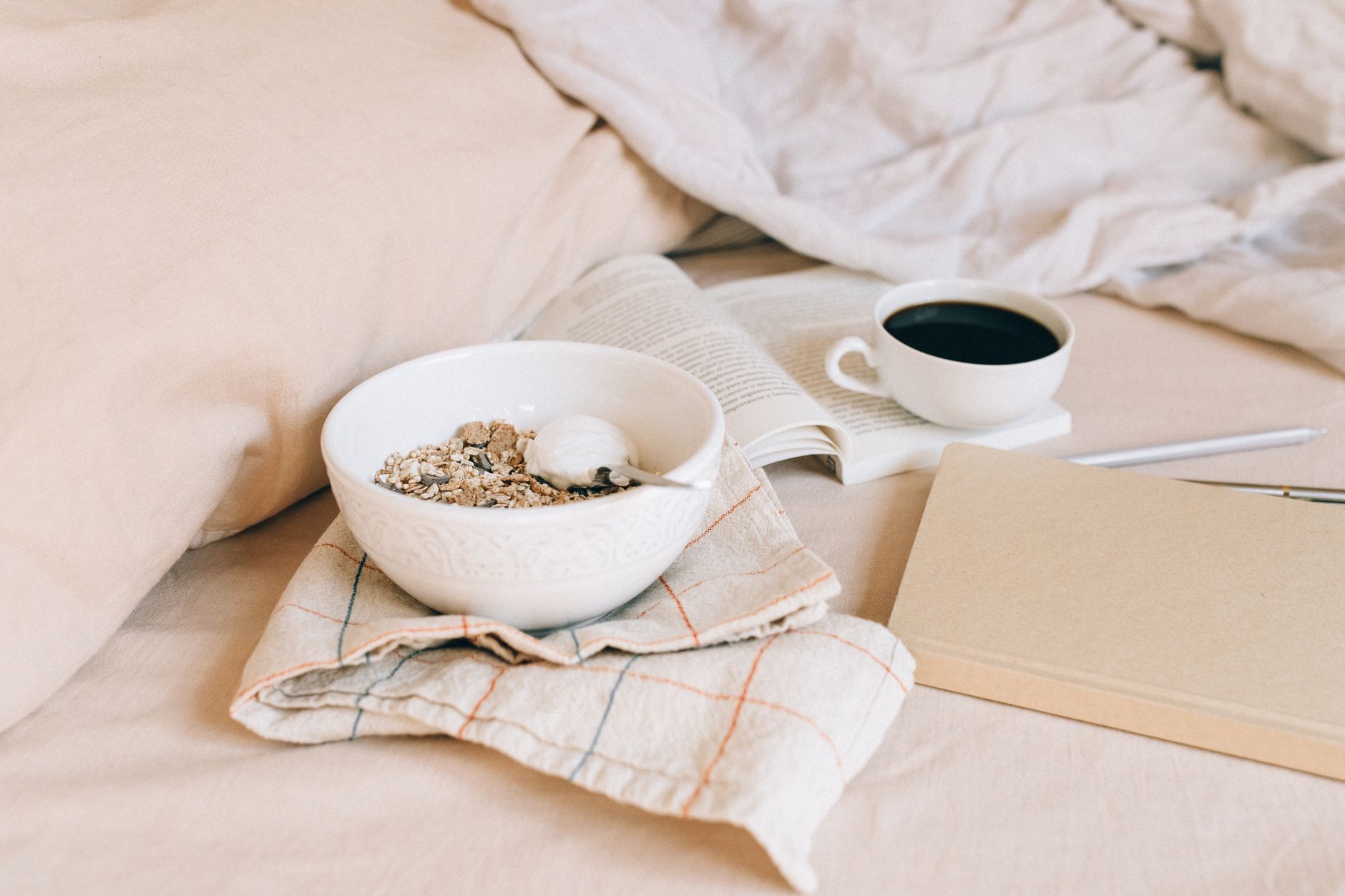 A cozy morning scene featuring a bowl of granola, coffee, and an open book on soft fabrics.