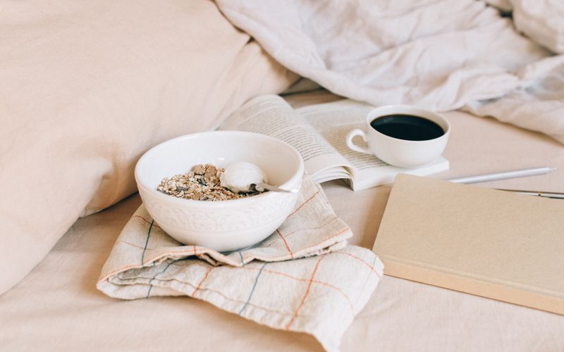 A cozy morning scene featuring a bowl of granola, coffee, and an open book on soft fabrics.