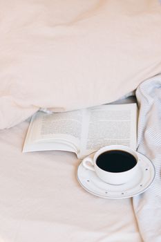 A cozy scene of a cup of coffee and an open book resting on a bed, capturing relaxation and comfort.