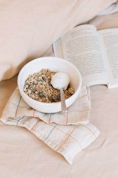 A calming morning scene featuring a bowl of granola beside an open book on a bed, perfect for relaxation.