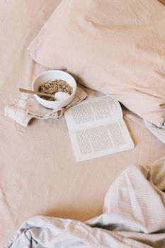 A cozy flat lay featuring an open book, bowl of granola, and soft fabric setting for a relaxing morning.
