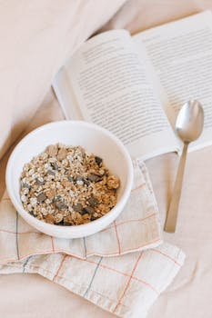 Relaxing breakfast in bed with a bowl of granola and an open book, perfect for a cozy morning.