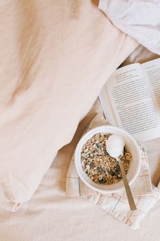 A serene morning setup with granola bowl, open book, and pillow for a relaxing breakfast in bed.