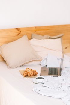 Comfortable morning in bed with croissants, coffee, and laptop, ideal for relaxation.
