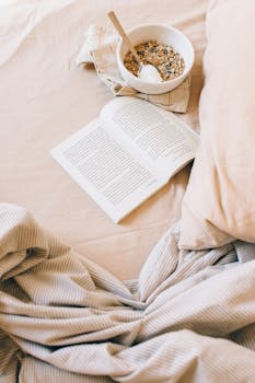 Comfortable morning setting with open book and granola bowl on bed.