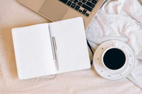 Free Cozy workspace setup with a laptop, notebook, and coffee cup on a soft blanket. Stock Photo