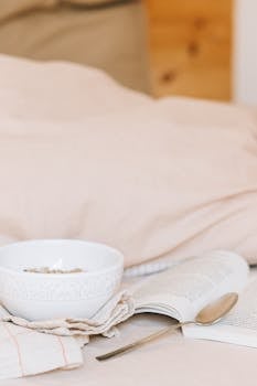 A bowl of granola and an open book on a cozy bed, perfect for a relaxing morning.