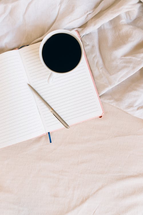 A Pen and a Cup of Coffee on an Open Notebook