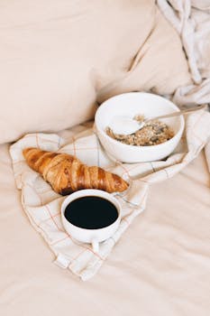 A warm, inviting breakfast in bed with coffee, croissant, and granola.