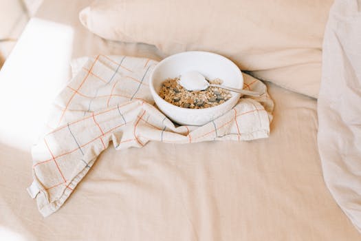 A bowl of granola with yogurt on a bed, exuding a cozy morning ambiance.