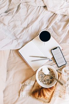Flat lay of breakfast with coffee, granola, and croissant on a bed.