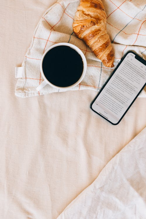 Free Cup of Coffee near a Croissant and a Cellphone Stock Photo
