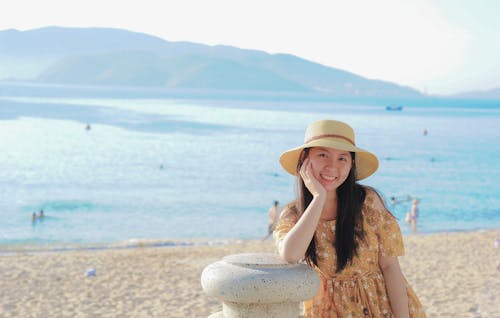 бесплатная Женщина в желтом цветочном платье и шляпе от солнца на пляже Стоковое фото