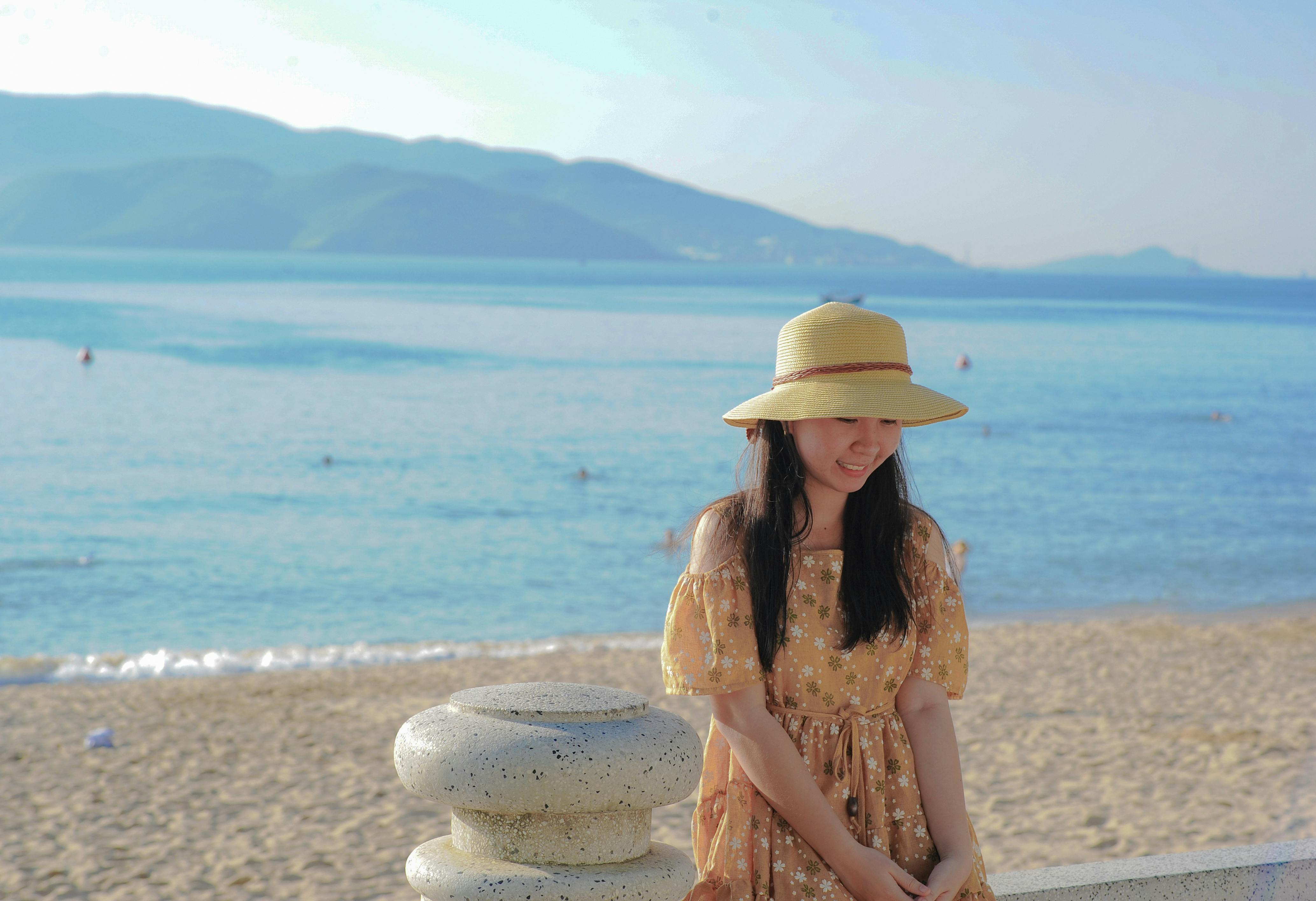 Smiling woman in a summer dress and hat enjoys a sunny day on a beach by the ocean.