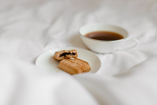A cozy morning scene with coffee and a bitten cookie on a white bed.