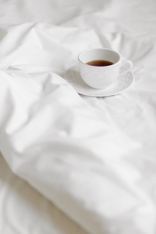 Free A white ceramic cup of coffee sits elegantly on a stylish bed with a bright blanket. Stock Photo