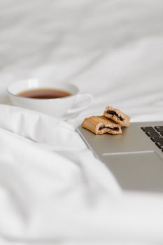Cozy setup with tea and cookies on a bed beside a laptop, perfect for relaxation.