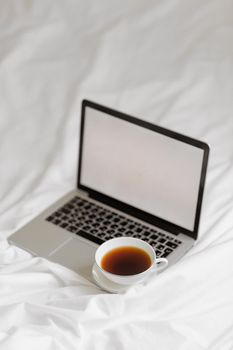A cup of coffee next to a laptop on a soft white blanket, creating a cozy workspace vibe.