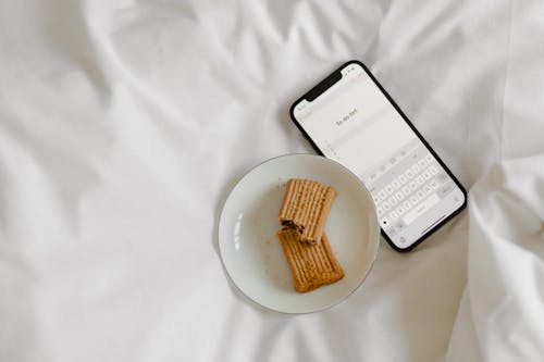 Brown Cookies on White Ceramic Plate beside Black Mobile Phone