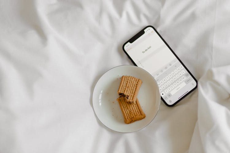 Brown Cookies On White Ceramic Plate Beside Black Mobile Phone