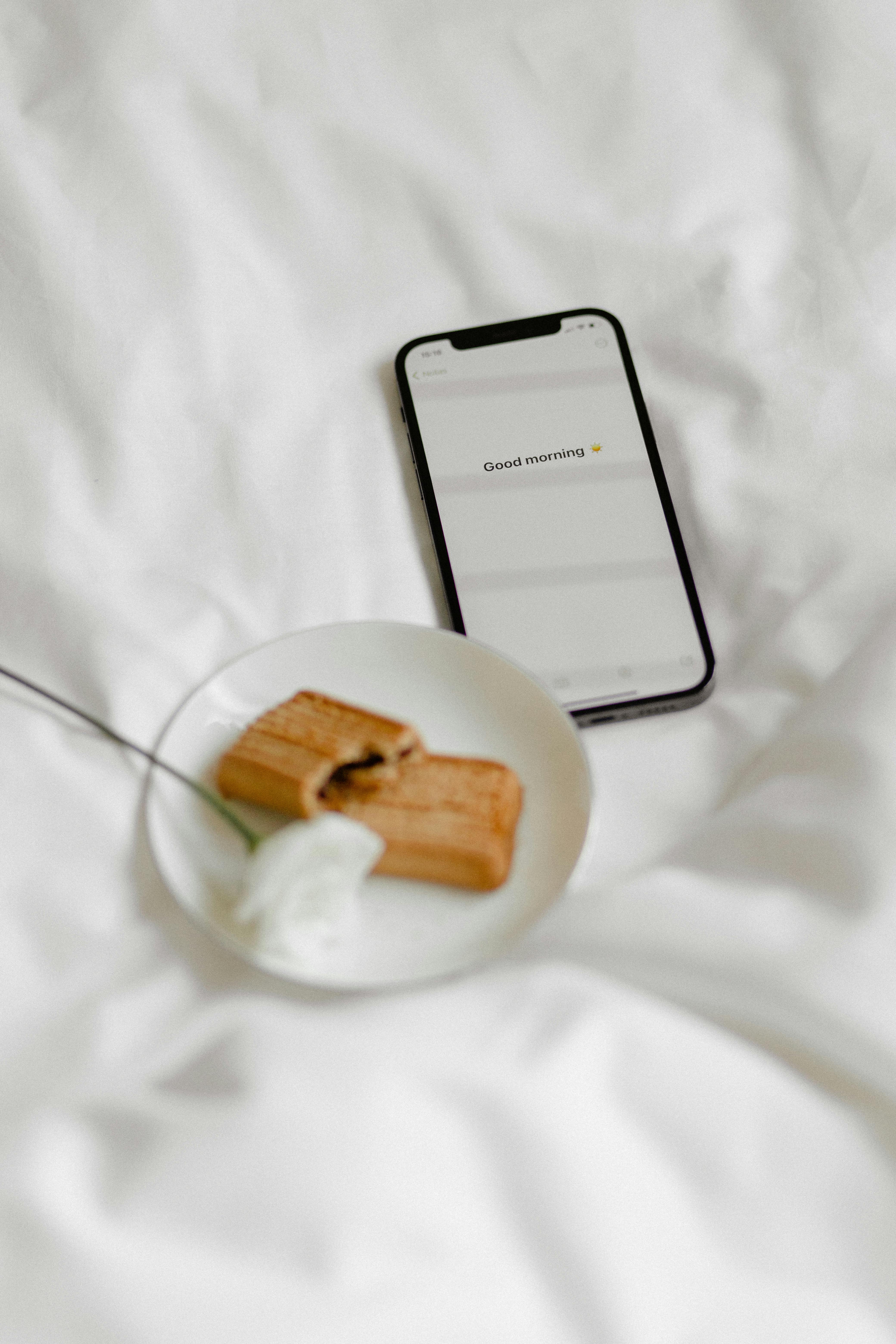 A cozy morning setup with a smartphone, biscuits, and a flower on a white blanket.