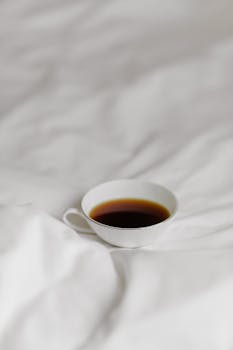 A simple coffee cup placed on soft white bedding, exuding a minimalist aesthetic.