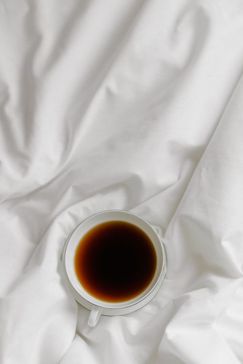 Free Minimalist photo of a black coffee cup resting on a white linen cloth. Stock Photo