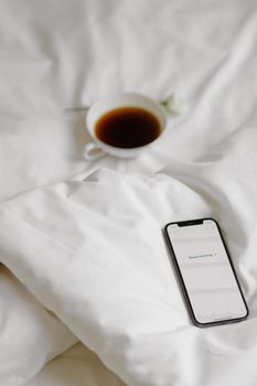 A serene morning scene with a smartphone and coffee cup on a soft white bed.