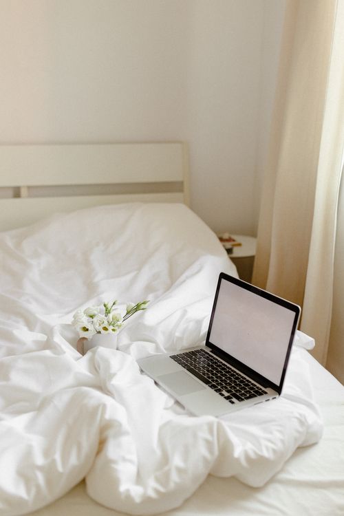 Free A cozy bedroom scene featuring a laptop, fresh white flowers, and soft bedding to depict relaxation and comfort. Stock Photo
