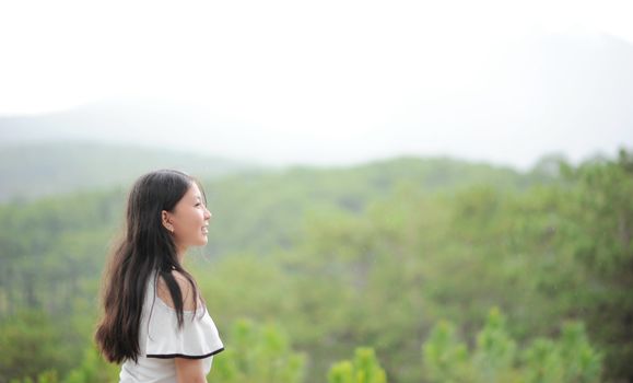 一名年轻女子微笑着站在薄雾笼罩的宁静森林中