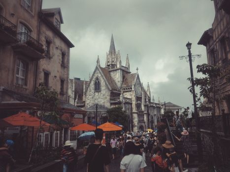 一座哥特式复兴教堂坐落在繁忙的城市中，阴天里可见游客和鲜艳的雨伞