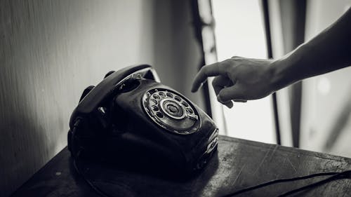 Grayscale Photo of Rotary Telephone Beside Person Hand