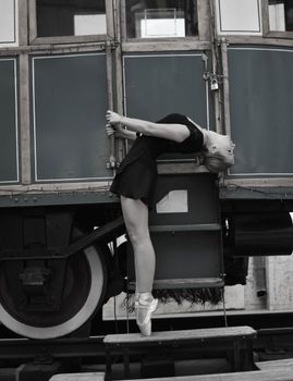 Ballet dancer performing en pointe arching pose beside an old tram.